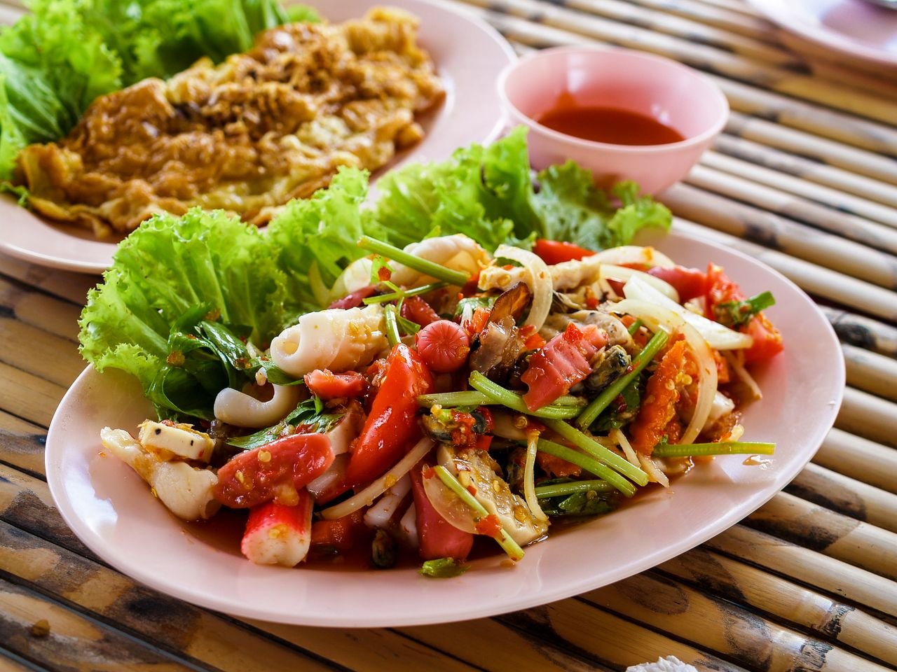 Authentic Thai seafood salad with fresh vegetables and herbs served on a pink plate.