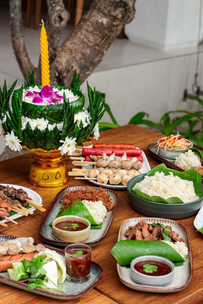 A colorful Thai meal setup with traditional floral decorations on a rustic wooden table.