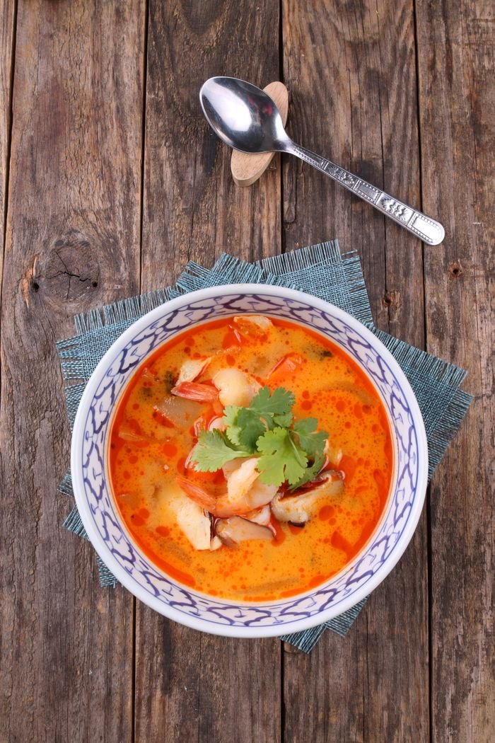 Traditional Thai tom yum goong soup with prawns, cilantro, and mushrooms in a decorative bowl.